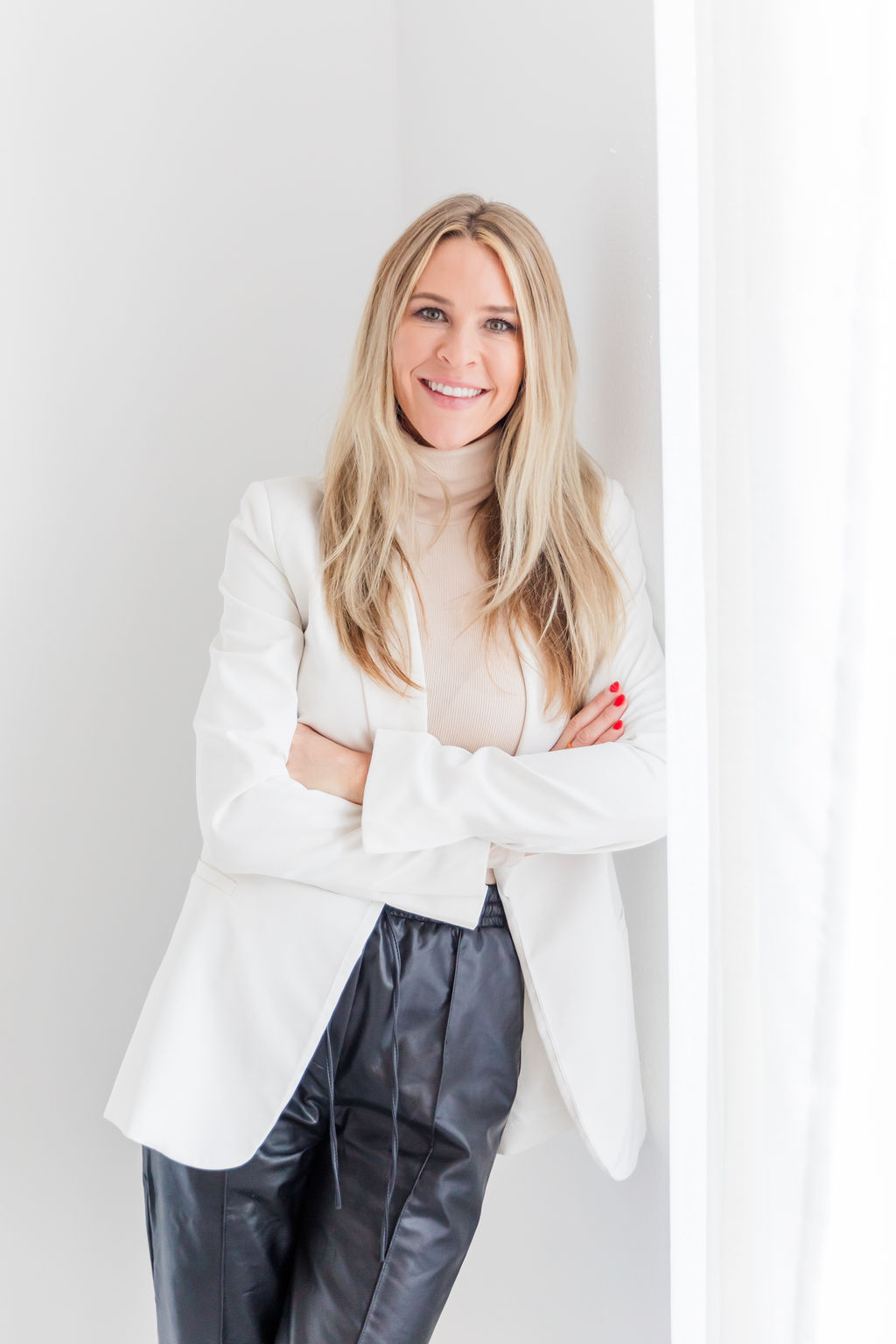 Chelsea Cadwell executive recruiter for Intoto Talent Recruiting standing again white wall in white blazer and black leather joggers